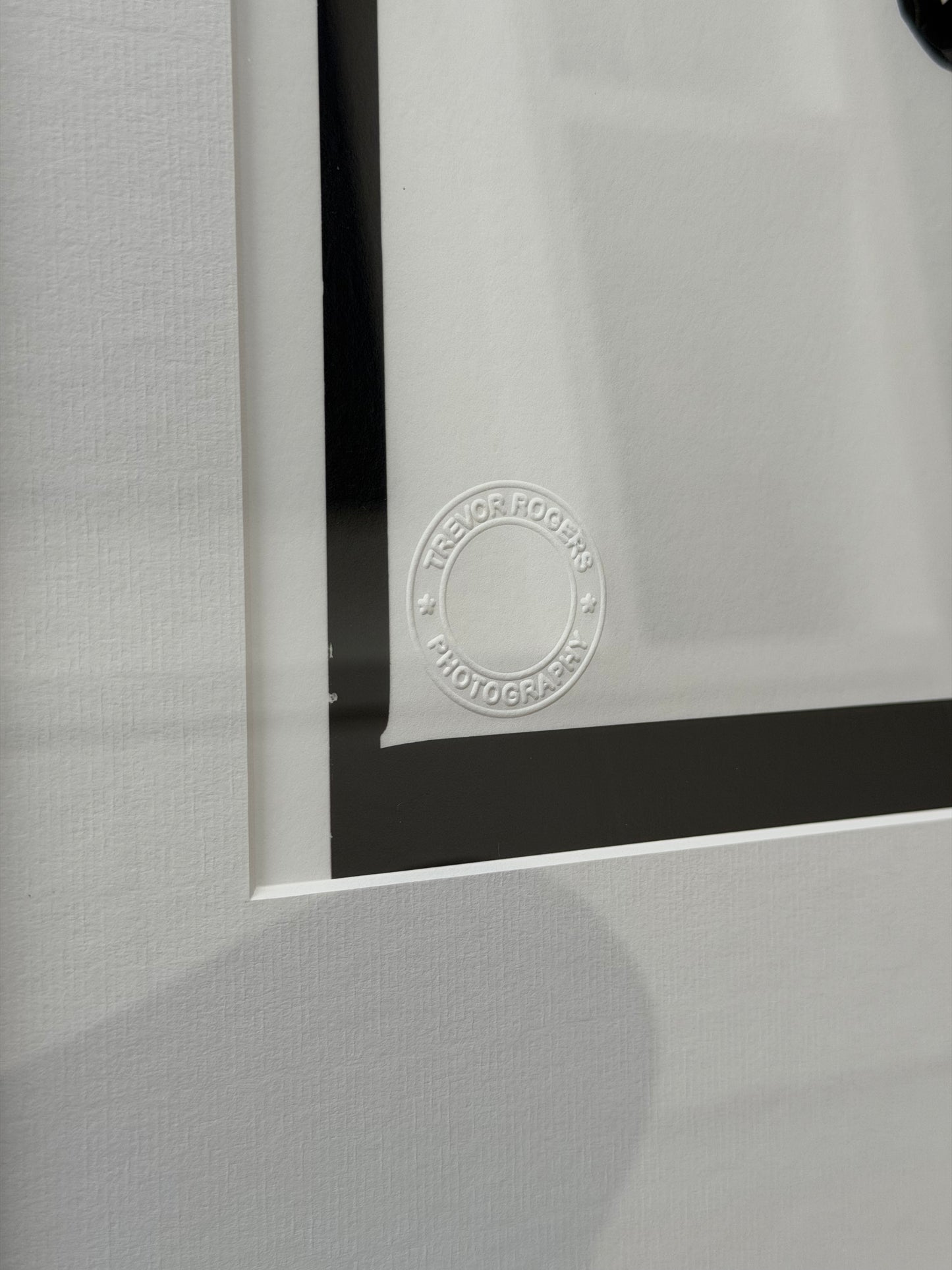Close-up of a framed photograph with a visible signature on a gray textured background